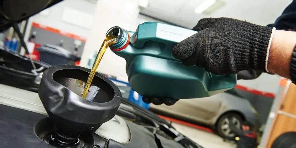 Pouring engine oil into a car engine with a funnel in a garage setting.