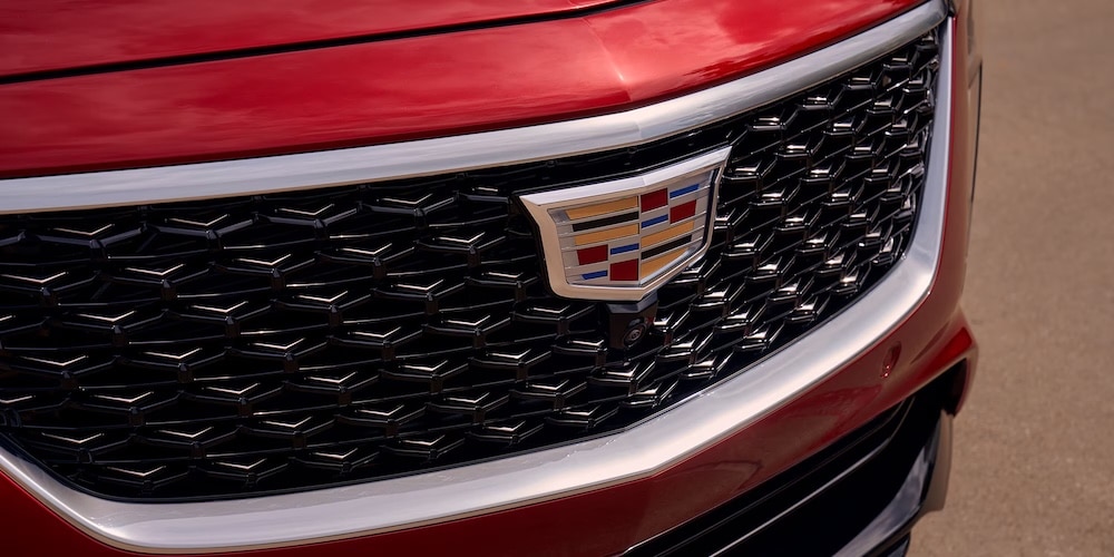 Close-up of a red luxury car grille featuring the Cadillac logo in sunlight.