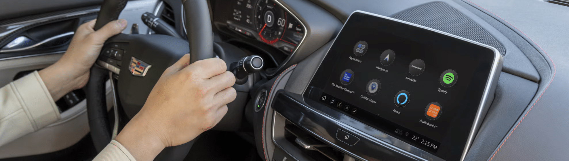 Driver handling a steering wheel with a dashboard touchscreen displaying app icons in a Cadillac.