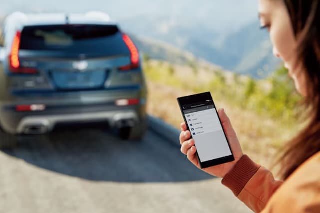 Person using a smartphone app near a parked SUV on a scenic mountain road.