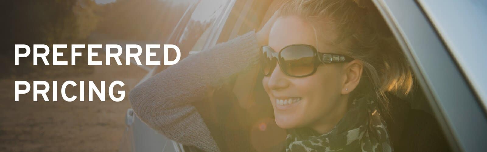Smiling woman with sunglasses in car window, with "Preferred Pricing" text on left. Sunny outdoor scene.