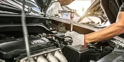 Mechanic wearing gloves uses a wrench to repair a car engine in a well-lit garage.