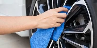 Hand cleaning a car wheel rim with a blue microfiber cloth, focusing on detailing.