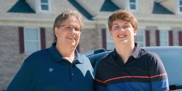 Two people smiling in front of a suburban house with a car nearby.