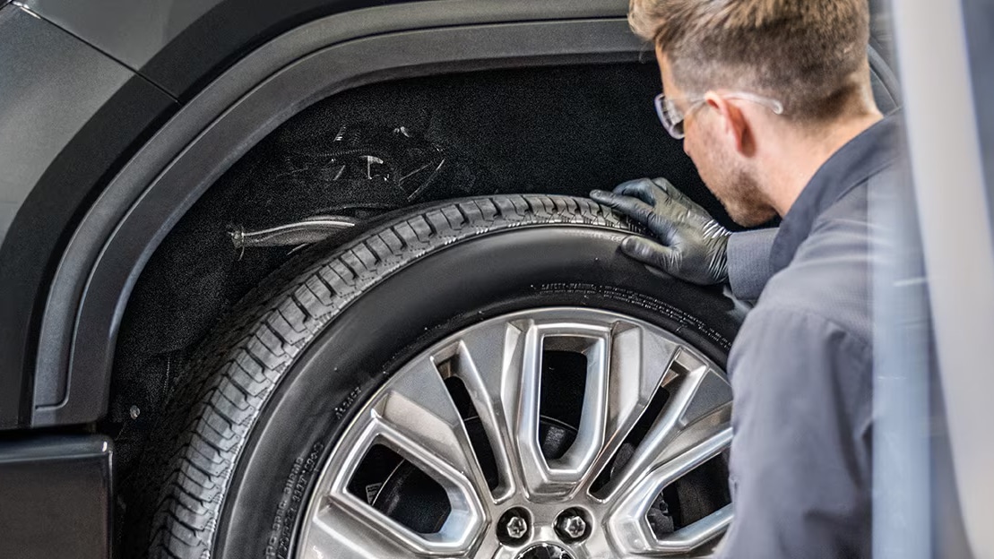 Mechanic inspecting a car tire for wear and damage in a workshop.