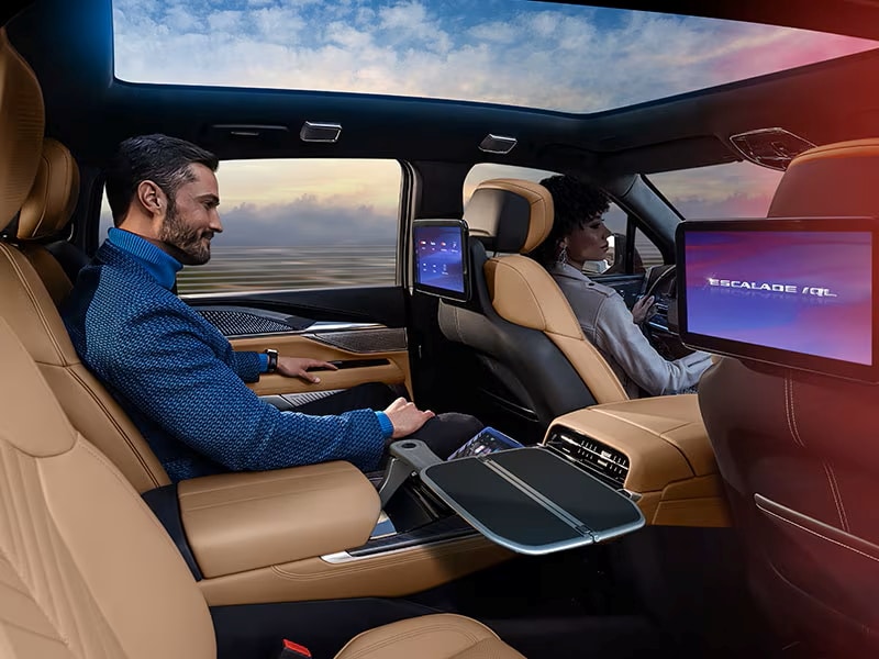Luxurious car interior with two passengers, touchscreen displays, and a panoramic sunroof during sunset.