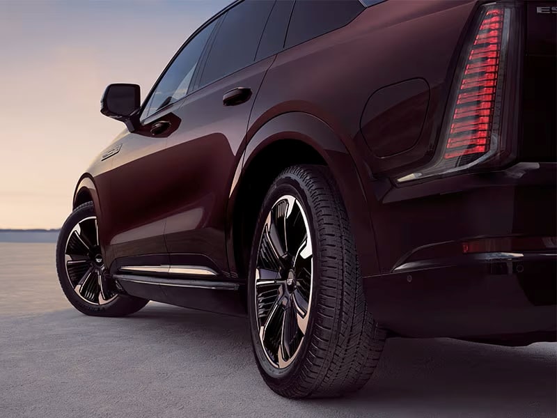 Close-up of a sleek black SUV with modern taillights at sunset, highlighting the shiny wheel rims.