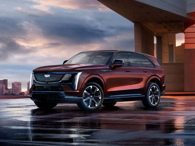 A sleek red SUV parked under an urban structure at dusk, with cityscape in the background.