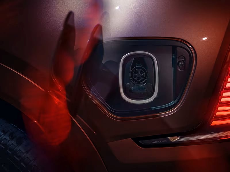 Electric car charging port on a Cadillac vehicle, illuminated by red and ambient lighting.