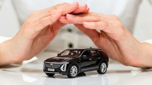 Hands gently cover a miniature black SUV car model, symbolizing car protection.